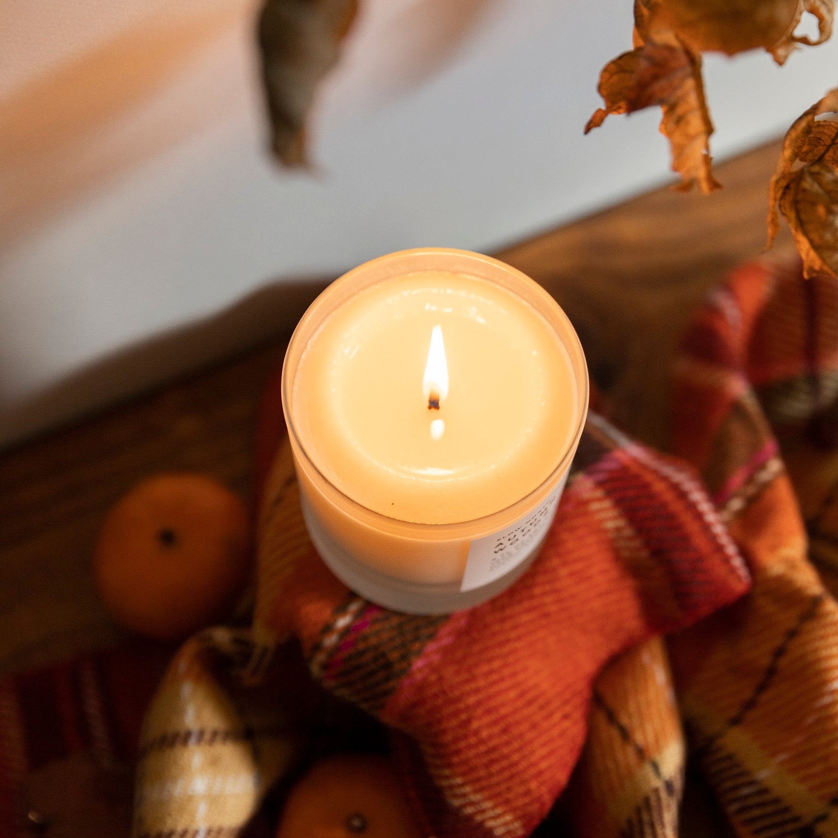 overhead view of a lit candle surrounded by brown leaves and a red flannel fabric