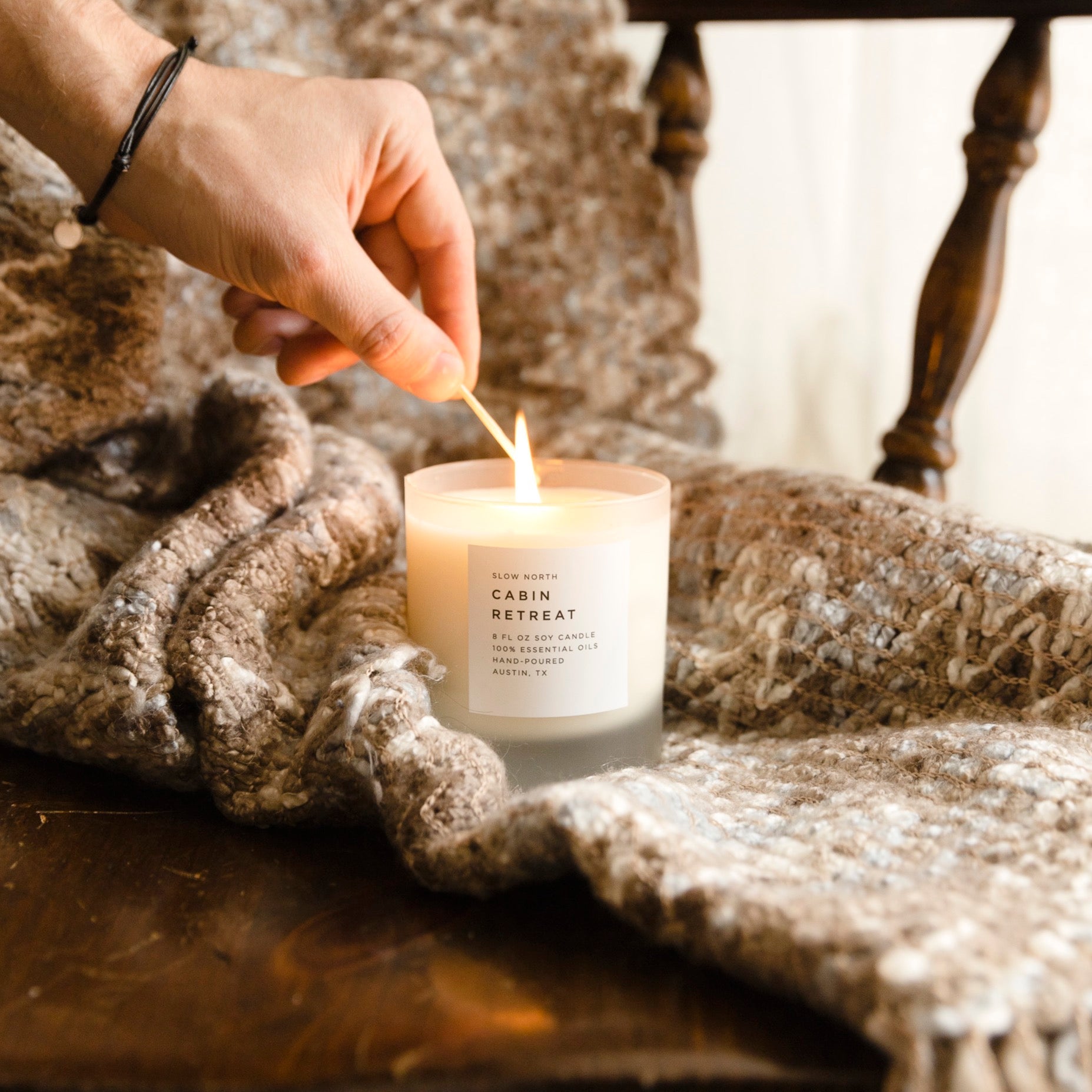 hand lighting wick on white soy wax candle, featuring Cabin Retreat by Slow North