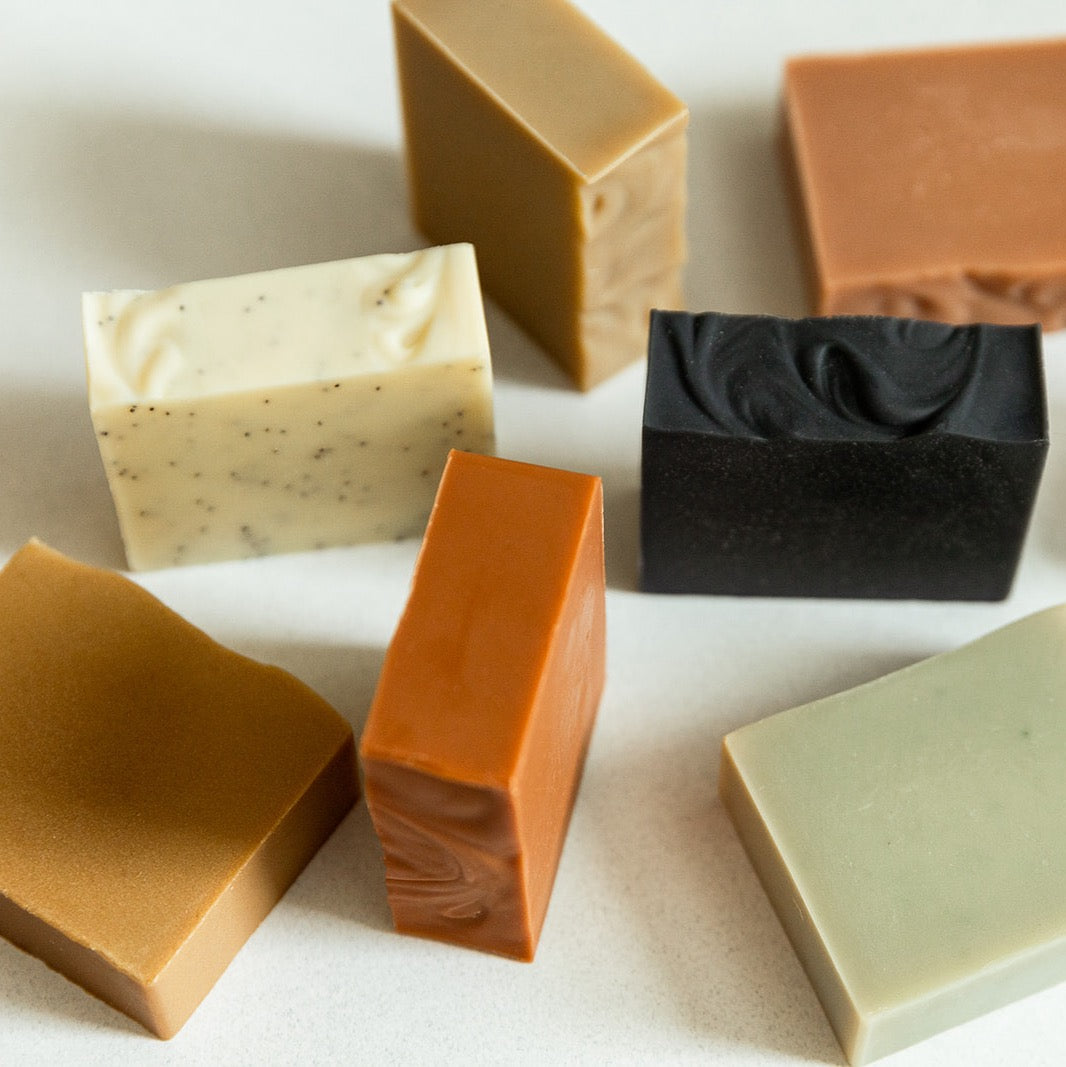 Seven Slow North bar soaps in different colors. Soaps are in muted shades of tan, green, and red, black on a white surface.