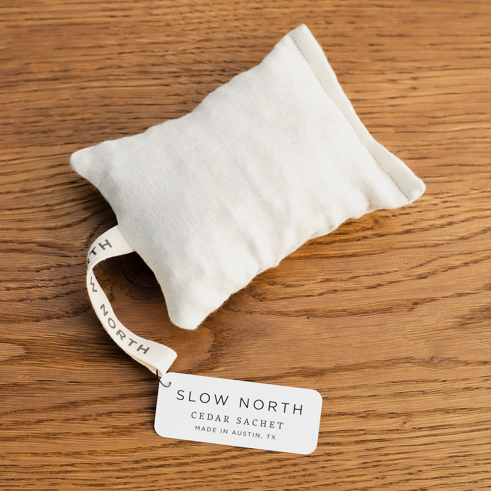 A close-up of a rectangle natural cotton herbal sachet that is an off-white cloth and filled with cedar chips.